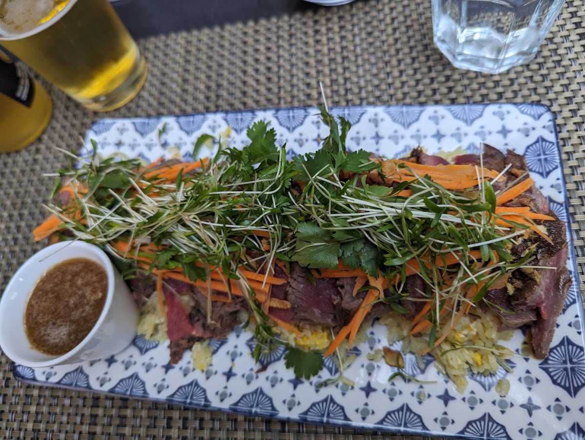Tataki de bœuf en terrasse, herbes et carottes, servi avec une bière fraîche.